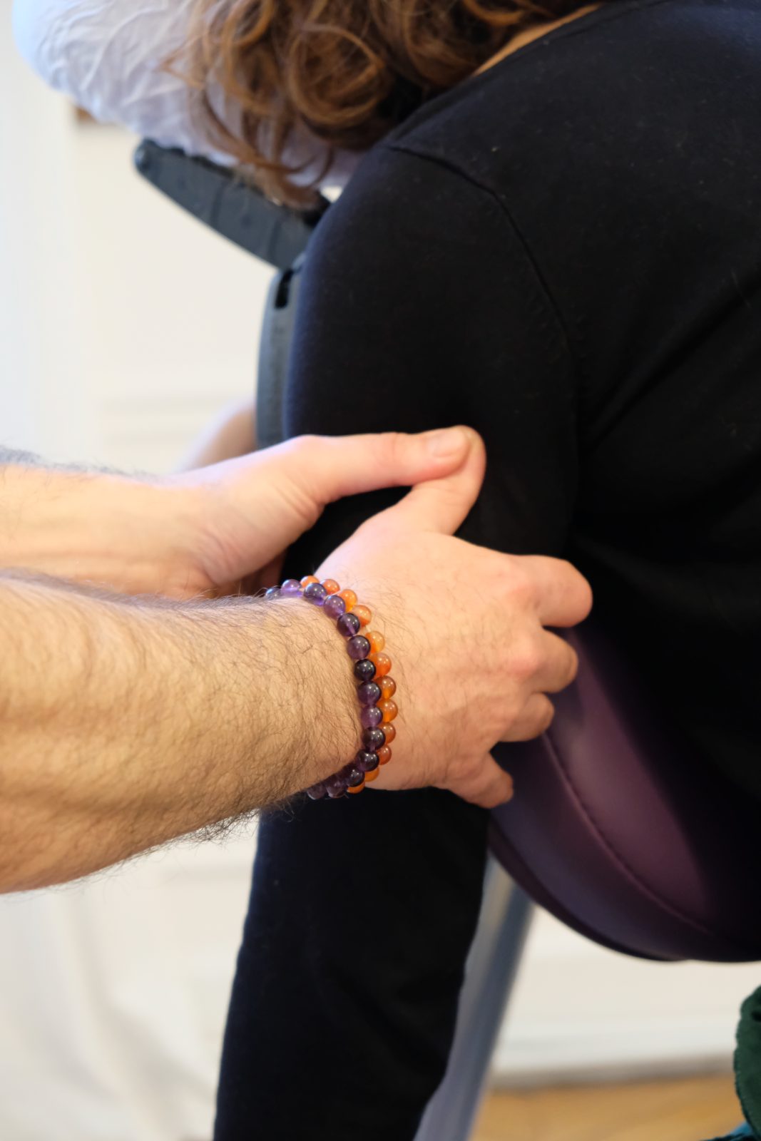 Mains posées sur l’épaule d’une cliente, bracelet d’améthyste et de cornaline